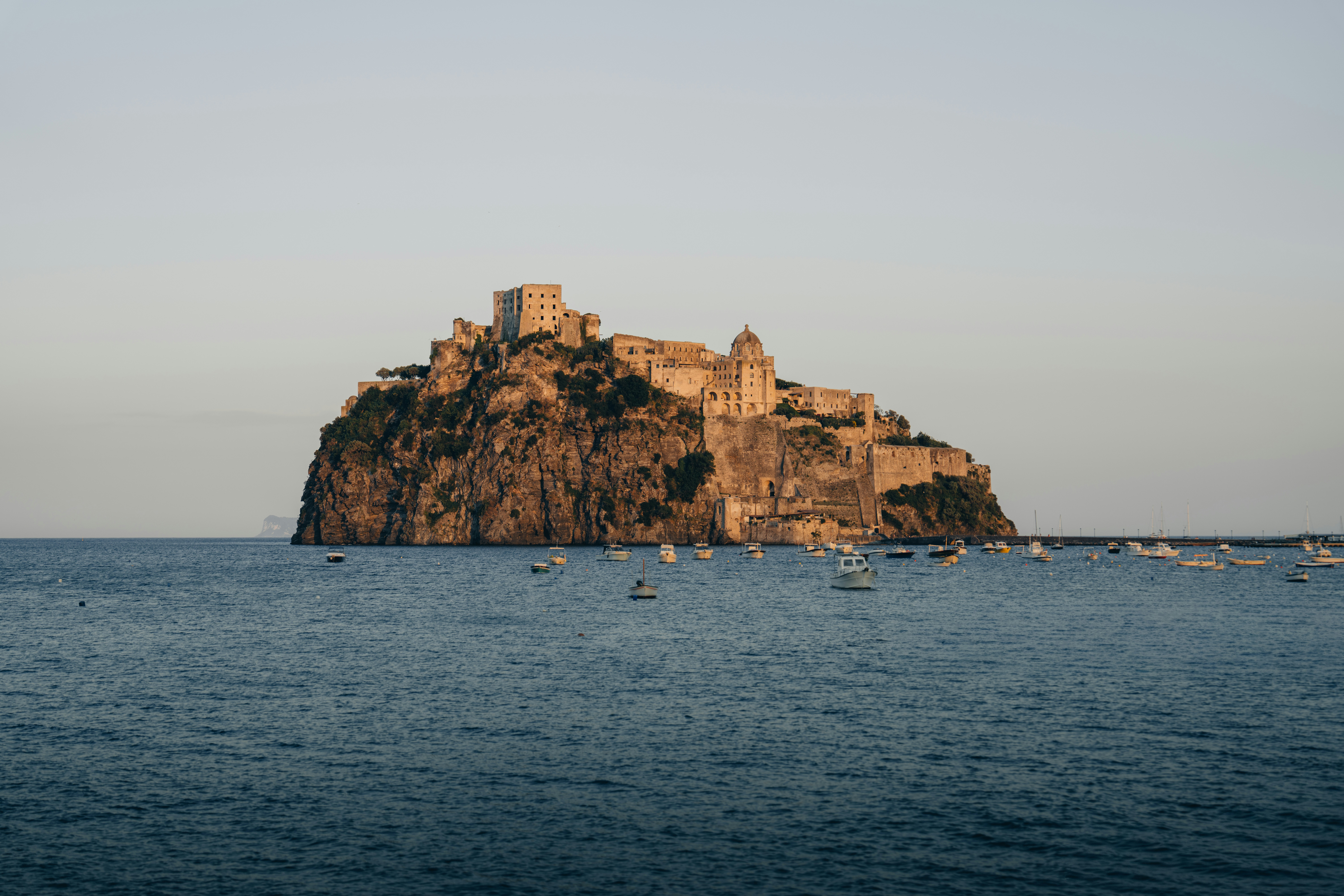 Historic castle on rocky island with boats in blue sea.